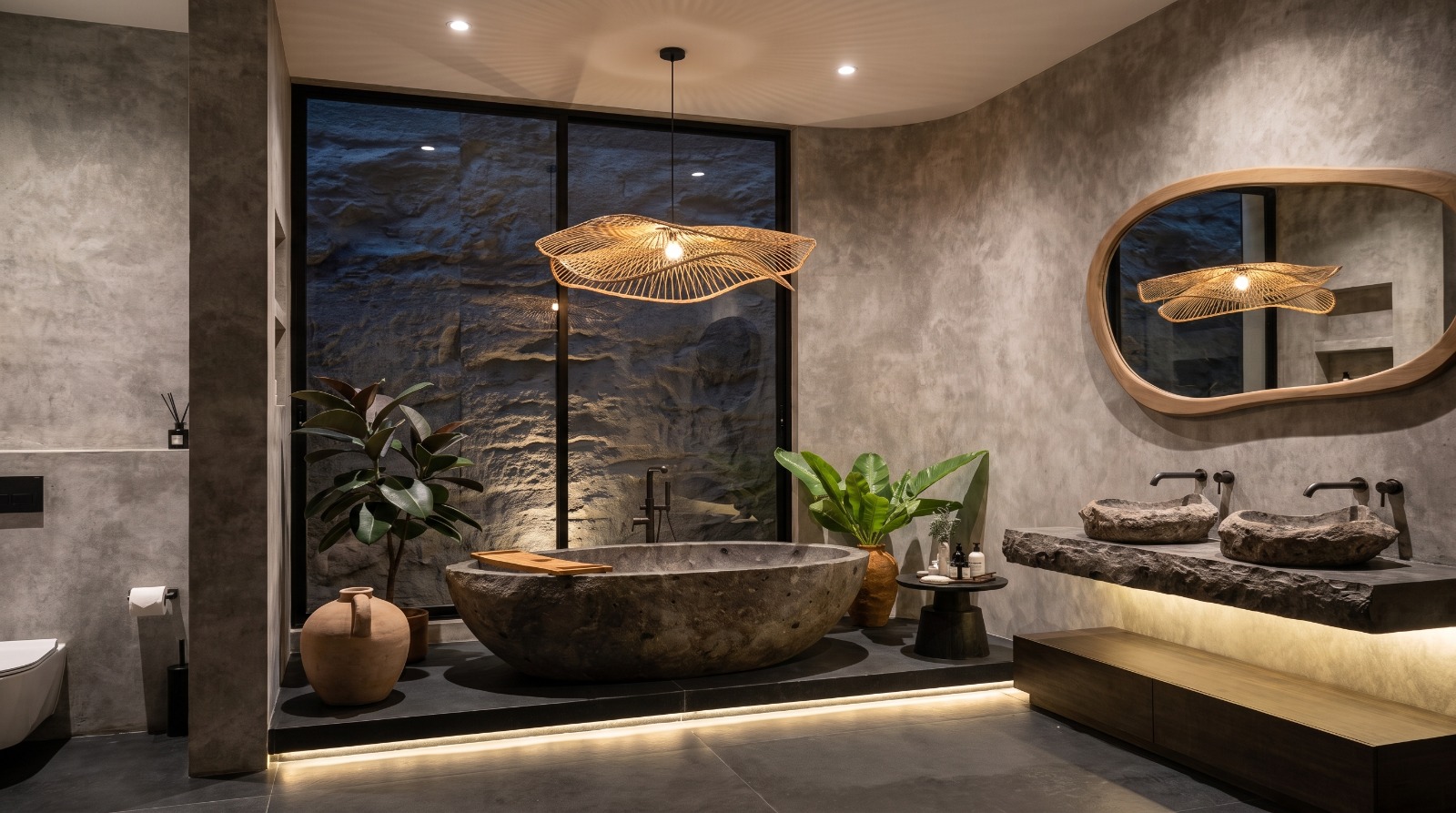 Master bathroom with carved stone bathtub, twin stone basins and lit rock wall